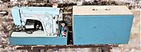 Side view showing the turquoise Kenmore sewing machine seated in its base with matching turquoise cover next to it.