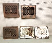 Five matching antique wall grates displayed on pegboard, showing differences in paint wear and patina