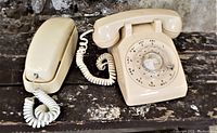 Photo of two ivory colored retro telephones, one rotary dial Western Union and one push button Bell, on a rustic wooden surface.