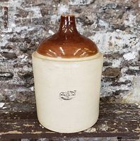 Front view of large antique Medalta jug with cream body and brown glazed top, showing oval Medalta Stoneware Ltd Medicine Hat stamp on front.