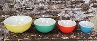 Photo of four vintage Pyrex graduated bowls in yellow, green, red, and blue against a rustic stone background, showing size and color progression.