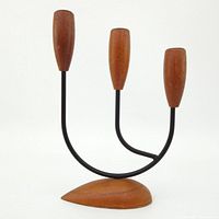 Front view of the three-arm candle holder showing teak candle cups on black metal arms and carved teak base