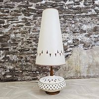 Full view of lamp showing base, wood column, and tall shade against stone background