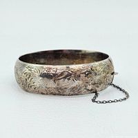 Oblique view of sterling silver bangle showing engraved floral and foliate designs on white background
