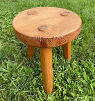 Front angle showing round thick wooden stool top and one leg firmly planted on grass.