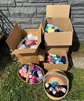 Five cardboard boxes and two woven baskets filled with yarn skeins displayed outdoors