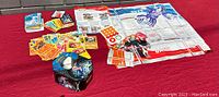 Photo showing a spread of Pokemon cards, a Pokemon storage tin, a game play mat with colorful character images and markings.