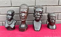 Four carved African bust sculptures displayed side by side with varying detailed facial features and hairstyles.