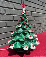 Full view of vintage ceramic Christmas tree showing green branches with snow-covered tips and multiple red birds attached, sits on dark base with power cord.