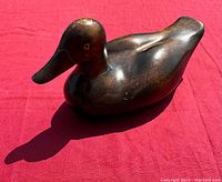 Side view of vintage wooden duck decoy showing carved details and surface wear.