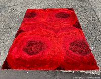 Overhead shot of entire rectangular red shag rug showing stylized lotus flower design in contrasting red and black tones, texture, and pile depth.