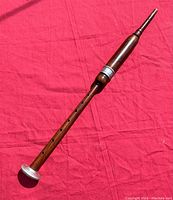 Full view of one wooden pipe with finger holes and silver-colored metal ring on red background.