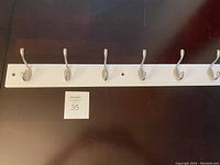 Front view of the white wooden coat hook rack with six silver metal hooks attached evenly spaced along the length.