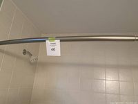 Curved metallic shower bar mounted on tiled shower walls with a visible mounting bracket on the right side and a shower head attached to the wall on the left.