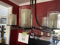 Close-up of 3 frosted cylindrical glass shades on black brown metal chandelier frame with a MaxSold tag.