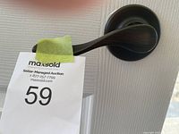 Photo of single black brown curved door handle mounted on door with auction lot tag