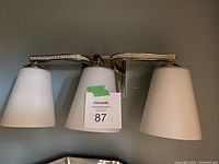 Three-light wall light fixture with polished metal frame and frosted glass shades, crystal band detail visible. Photograph shows fixture powered off.