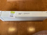 White sealed package labeled IKEA Mosslanda bookshelf, placed on a wooden floor.