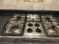 Kitchenaid 4-burner gas stove top with black metal grates and four control knobs on stainless steel surface