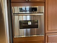 Full front view of the KitchenAid built-in electric oven installed in wooden cabinetry showing the door with a viewing window and stainless steel finish.