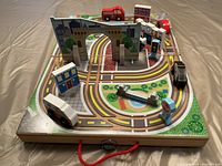 Top view of the open wooden playset showcasing road track, several small wooden buildings including a fire station, and wooden vehicles such as a fire truck and other cars.