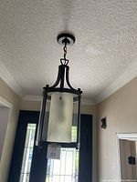 Full view of the black brown pendant light hanging from a ceiling showing textured ceiling and entryway background.