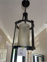 Pendant light hanging from ceiling showing black brown metal frame enclosing frosted glass shade.