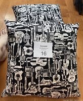 Two square pillows with black and white musical instrument pattern including guitars, saxophones, and pianos on a wooden floor.