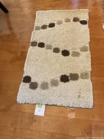 Full view of the beige rug runner showing the abstract pattern of brown and gray square dots in curved lines, placed on a hardwood floor.