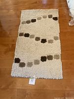 Full view of beige shag-style rug runner with square patch wavy line design in browns and gray on wooden floor.