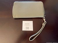 Closed olive color Thirty One wallet with zipper and wrist strap on dark surface.