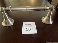 Toilet paper holder viewed from front showing the horizontal cylindrical bar and round mounting bases on a dark surface.