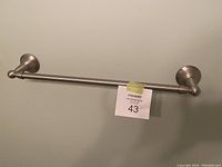 Photo of a mounted brushed nickel towel bar against a light wall, showing the entire bar and both mounting brackets with a MaxSold lot tag.