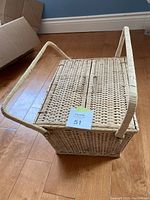 Closed wicker picnic basket on wooden floor showing rectangular shape, woven wicker texture, and wrapped handle.