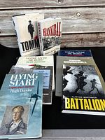 Photo showing seven military and historical themed books including Battalion, Winston Churchill, Tommy, Hannibal, Flying Start, and a French marine logbook.