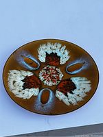 Front of the circular decorative plate showing intricate iridescent marbled pattern in gold, bronze, copper, red, white, and blue.