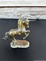 Front angle photo of a vintage brass unicorn figurine with a raised front leg on a textured base.