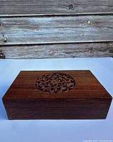 Closed view of the top of the wooden box showing the hand carved circular floral design in the center of the lid.