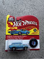 Front view of sealed Hot Wheels Authentic Commemorative Replica Blue die-cast car with included spare tire, on original blister card packaging highlighting 25th Anniversary logo and flame graphics.