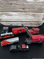 Photo showing multiple Lionel train cars including Texaco tanker, boxcar, crane car, locomotive, and caboose on black surface.
