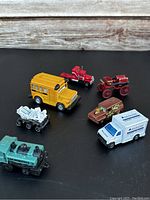 Seven miniature vehicles displayed on black background showing various vehicle types including school bus, armored vehicle, and vintage carriage.