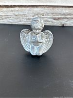 Front view of small painted terracotta angel figurine with detailed wings and praying hands, placed on a dark surface with wooden background.