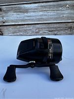 Side view of Shimano II black vintage fishing reel, showing handle and model markings.