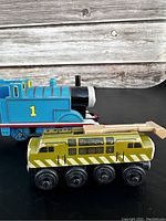 Side view of blue Thomas train engine and green Diesel 10 wooden train car on black surface