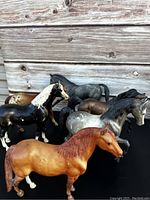 Six vintage Breyer model horses in various colors and poses against a wood backdrop.