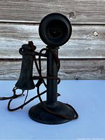 Front view of vintage black candlestick telephone with visible rust and attached earpiece on cord
