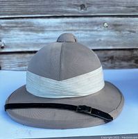 Front side view of a light brown safari hat with white band and black chin strap.