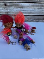 Multiple vintage Treasure Troll figures arranged on white surface against wooden plank background, showing large and small trolls with colorful hair and small animal figures.