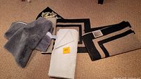 Four area rugs placed on a carpeted floor including a plush gray rug, a white folded rug, and two beige rugs with black and brown geometric border patterns.