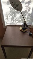 Square wooden end table with gold and black lamp on top, showing surface and lamp base.